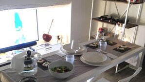 Uma área de refeições com uma mesa comprida posta para dois, uma salada e uma taça de vinho.