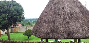 A thatched-roof structure with a green base, surrounded by a wooden fence and a small tree.