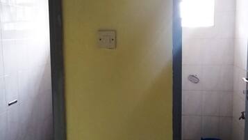 Ein Badezimmer mit weißen Fliesen, einer gelben Tür, einem Lichtschalter, einem Handtuchhalter und einer Duschkabine.