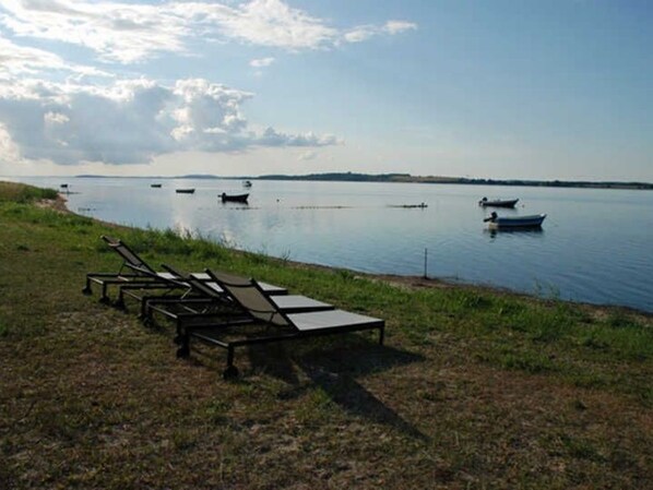 A lakeside setting with lounge chairs and boats on the water.