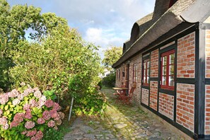 A brick building with a thatched roof, a stone pathway, and a table with chairs outside.