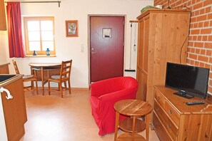 A room with a wooden cabinet, a television, a red chair, a small wooden table, and a window with curtains.
