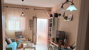 Sala de estar con sofá, mesa de centro y zona de televisión. Hay una mesa de comedor con sillas y una cocina con nevera y microondas.