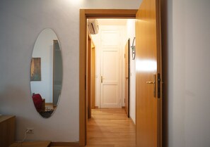 A hallway with a wooden door, a white wall, and a mirror reflecting a room with a red chair. - Cenisio apartment (Milan)