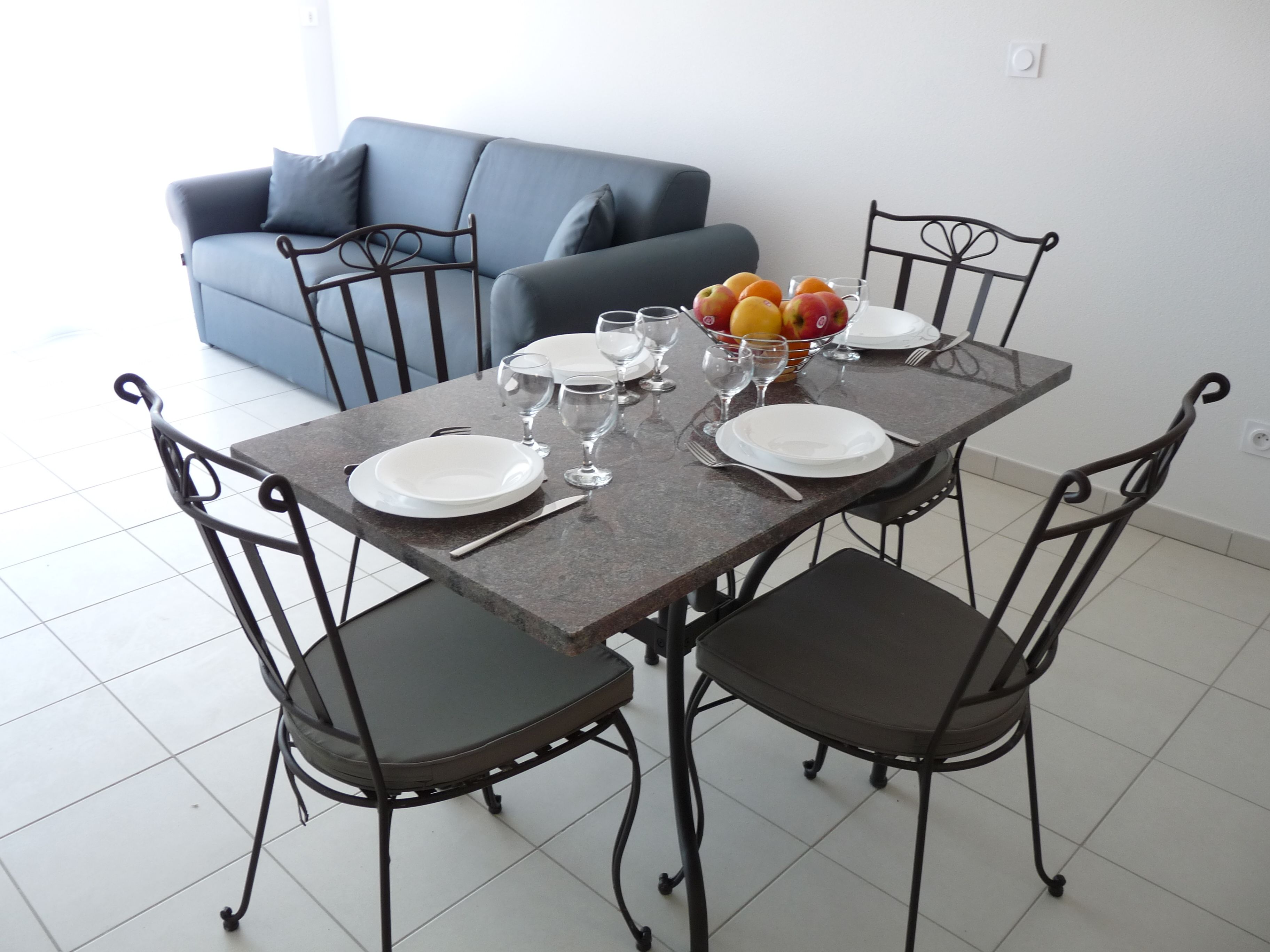 A dining table with four chairs, a bowl of fruit, and empty plates and glasses.