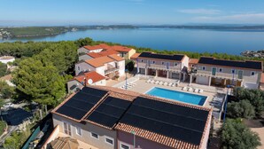 A residential area with a swimming pool, solar panels on rooftops, and a view of a lake. - Appart'hotel Résidence La Provence (Saint-Mitre-les-Remparts)