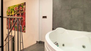 A bathroom with a large bathtub, a handrail, and a colorful painting on the wall. - Corso Buenos Aires 35 (Milan)