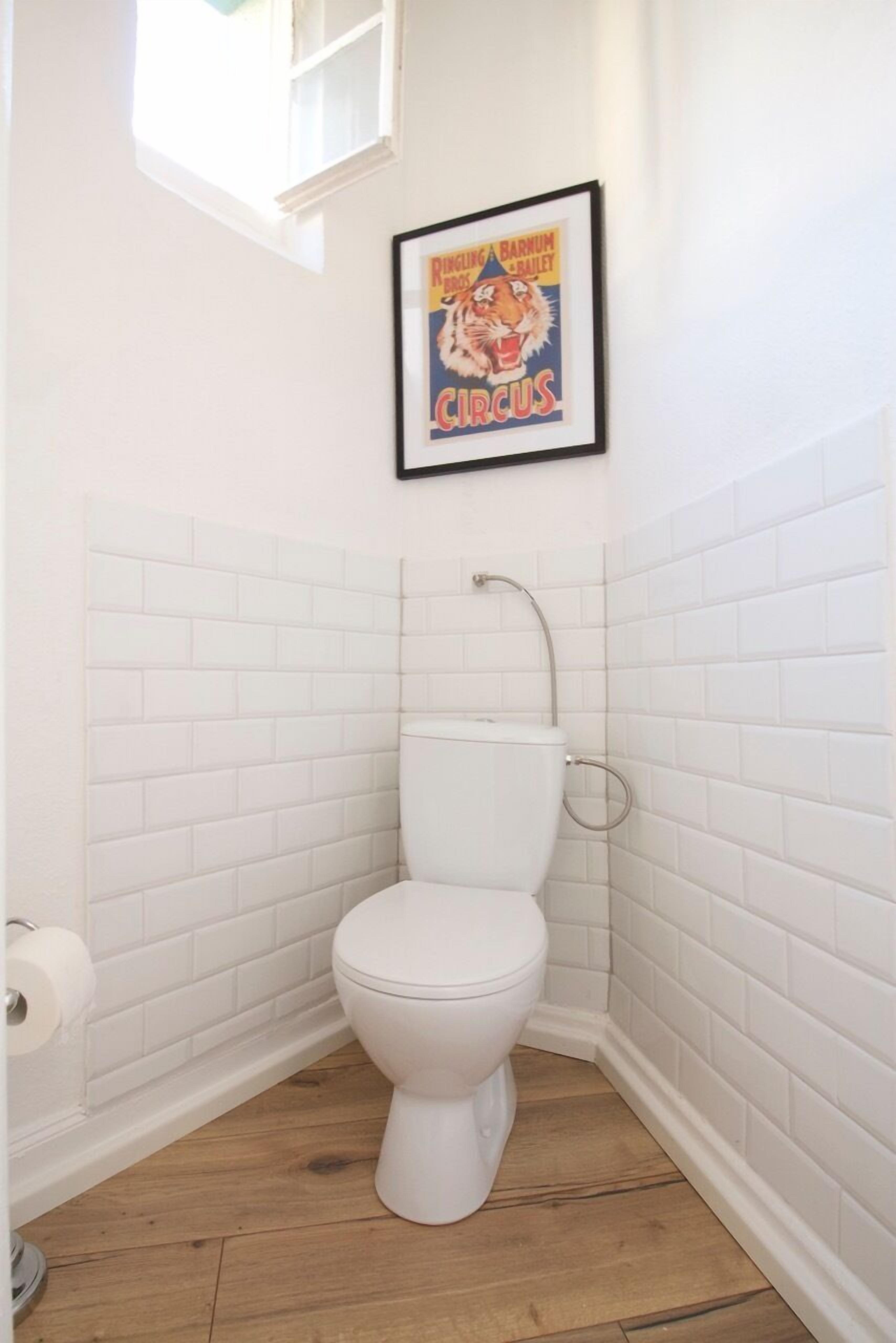 Un baño pequeño con un inodoro blanco, un rollo de papel higiénico y un póster enmarcados de un tigre de circo en la pared.