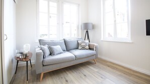 Una sala de estar moderna con un sofá gris, dos ventanas, una lámpara de pie y una mesita auxiliar.