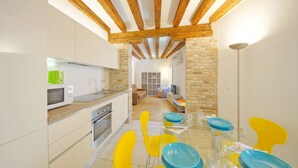 A modern kitchen with white cabinets, a microwave, and a dining area with yellow chairs and blue plates. - DolceVita Apartments N. 393 (Venice)