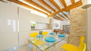 A modern kitchen with white cabinets, a glass dining table with yellow chairs, and a stone accent wall. - DolceVita Apartments N. 393 (Venice)