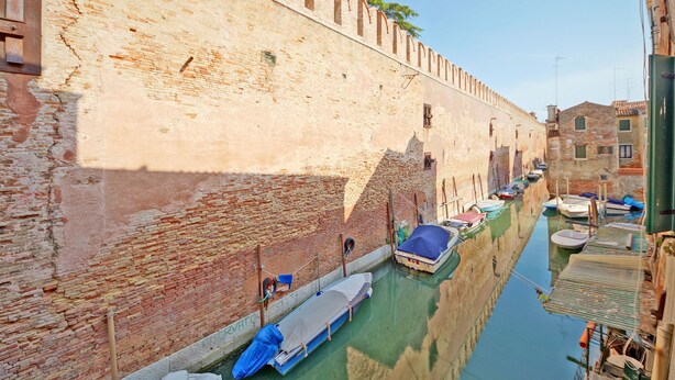 A narrow canal with boats docked along the walls, a brick wall with arched windows, and buildings with traditional architecture. - DolceVita Apartments N. 393 (Venice)