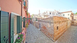 A narrow cobblestone street flanked by buildings with traditional architecture, including a church spire in the background. - DolceVita Apartments N. 393 (Venice)