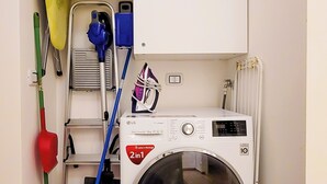 A laundry area with a front-loading washing machine, a drying rack, a mop, a broom, and a bucket. - Modular House - Alessandro (Cefalù)