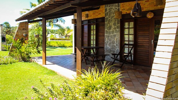 Un patio techado con mobiliario exterior, paredes de piedra y vistas a un jardín cuidado.