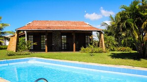 Una piscina con borde de azulejos, un muelle de madera y un edificio con techo de tejas y pilares de piedra.