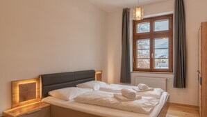 A bedroom with a bed, bedside tables, a window with curtains, and a radiator. - Post Residence Apartments 2B, sauna, SUMMER CARD (Zell am See)