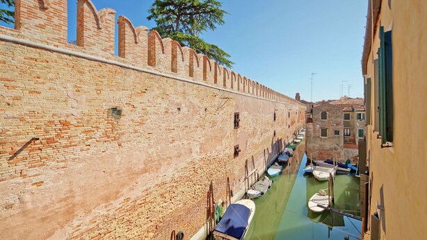 A narrow canal flanked by historic brick walls and buildings with small boats docked along the water. - DolceVita Apartments N. 394 (Venice)
