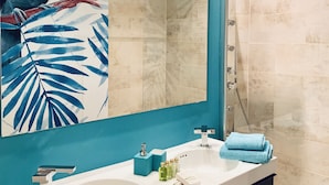Une salle de bain dotée d’un grand miroir, d’un lavabo, d’une douche et d’une fresque murale sur le thème des tropiques.