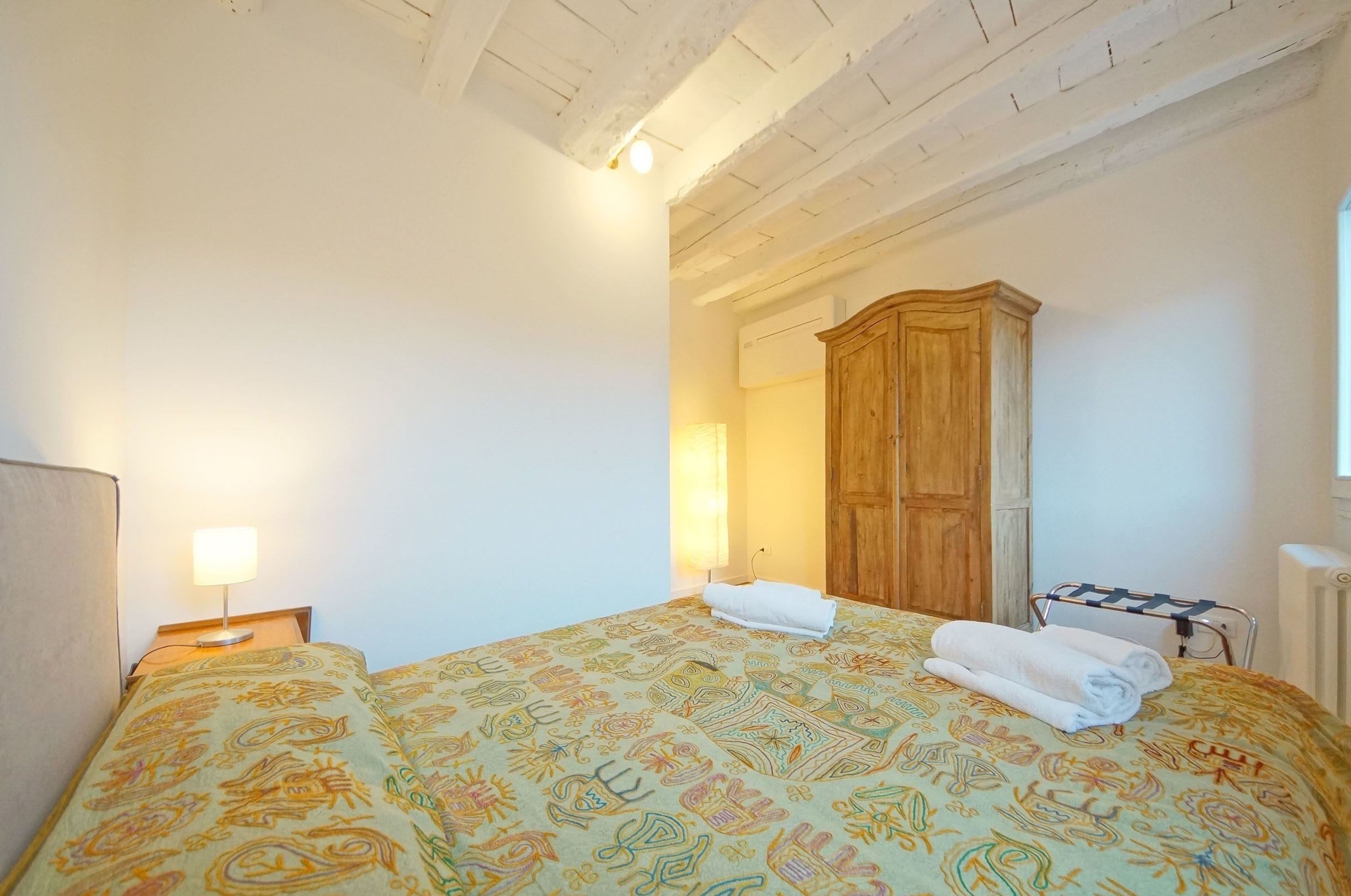 Ein Schlafzimmer mit einem Bett, einem Holzschrank, einem Nachttisch mit Lampe und einer Heizung.