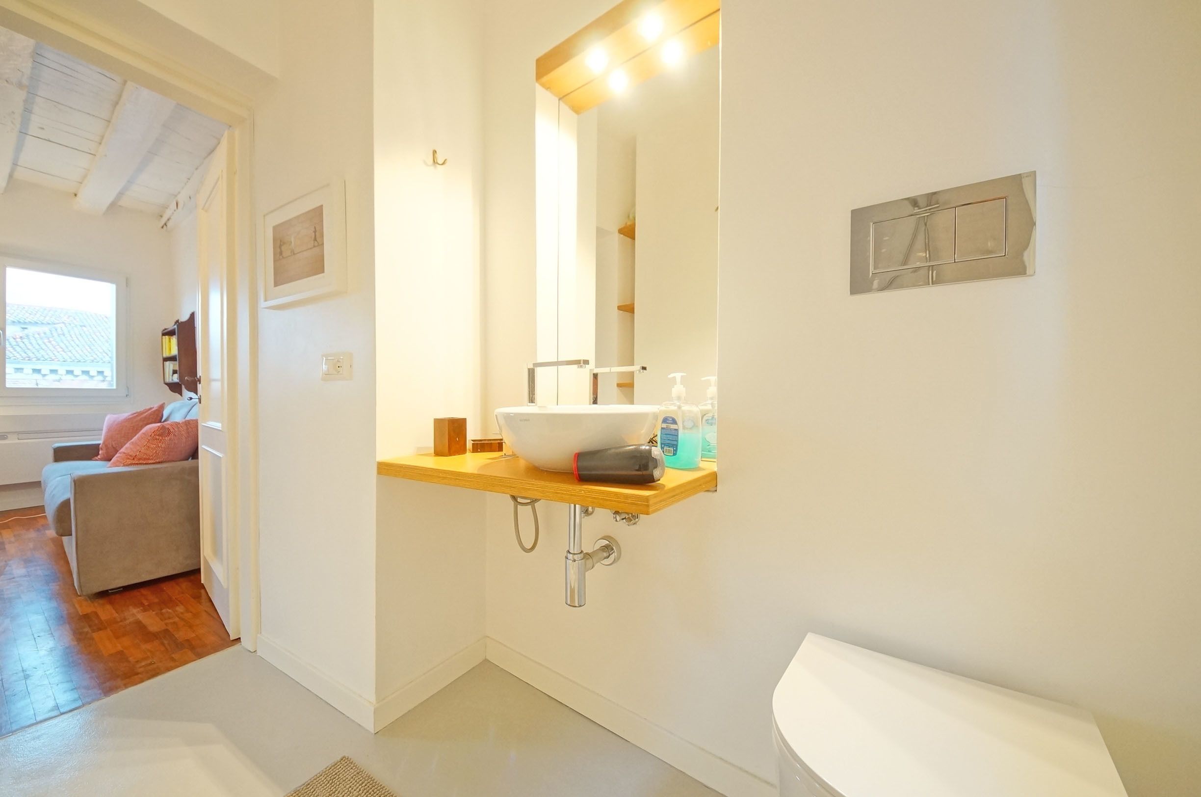 A bathroom with a white sink, wooden countertop, and a mirror. There is a towel rack on the wall and a window providing natural light.