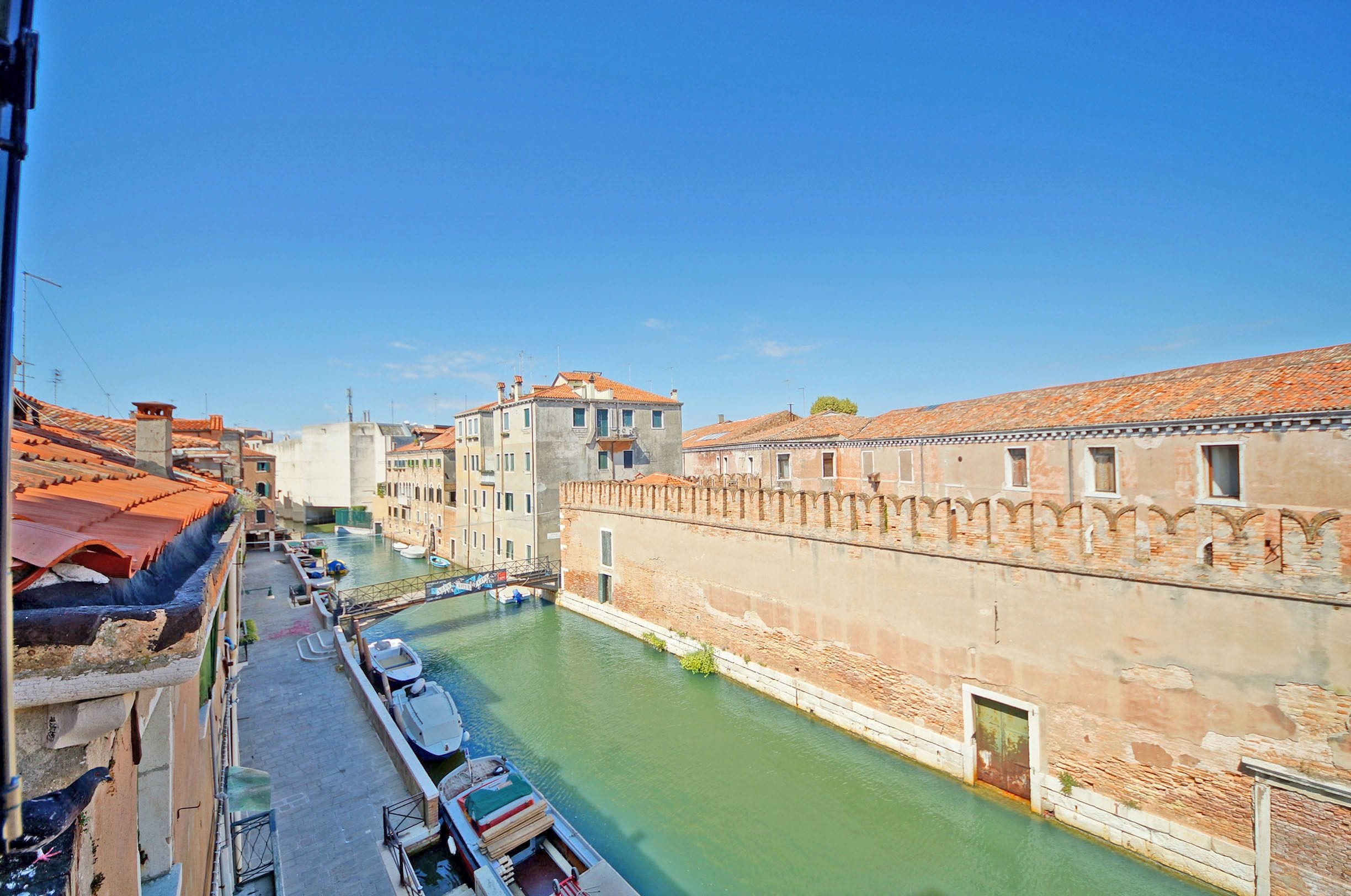 A canal with boats, historic buildings, and a clear blue sky.