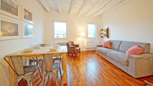 A dining area with a wooden table set for four, a sofa, and a lamp. - DolceVita Apartments N. 396 (Venice)