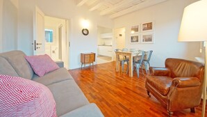 A living room with a sofa, a brown leather armchair, and a dining area with a table and chairs. - DolceVita Apartments N. 396 (Venice)