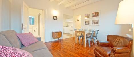 A living room with a sofa, a brown leather armchair, and a dining area with a table and chairs.