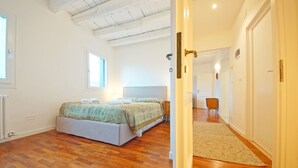 A bedroom with a bed, a wooden floor, a window, and a door leading to another room. - DolceVita Apartments N. 396 (Venice)