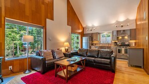 Ein modernes Wohnzimmer mit einem Ledersofa, einem roten Teppich und einem großen Fenster mit Blick auf einen Wald.