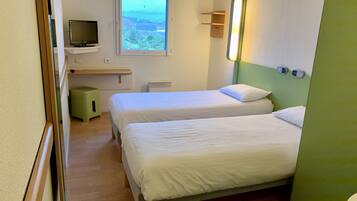 Habitación de hotel con dos camas, un televisor en un estante, una ventana con vistas y una lámpara fijada a la pared.