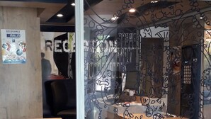Un espacio de oficina moderno con divisiones de vidrio, escritorios de madera y una silla de oficina negra.