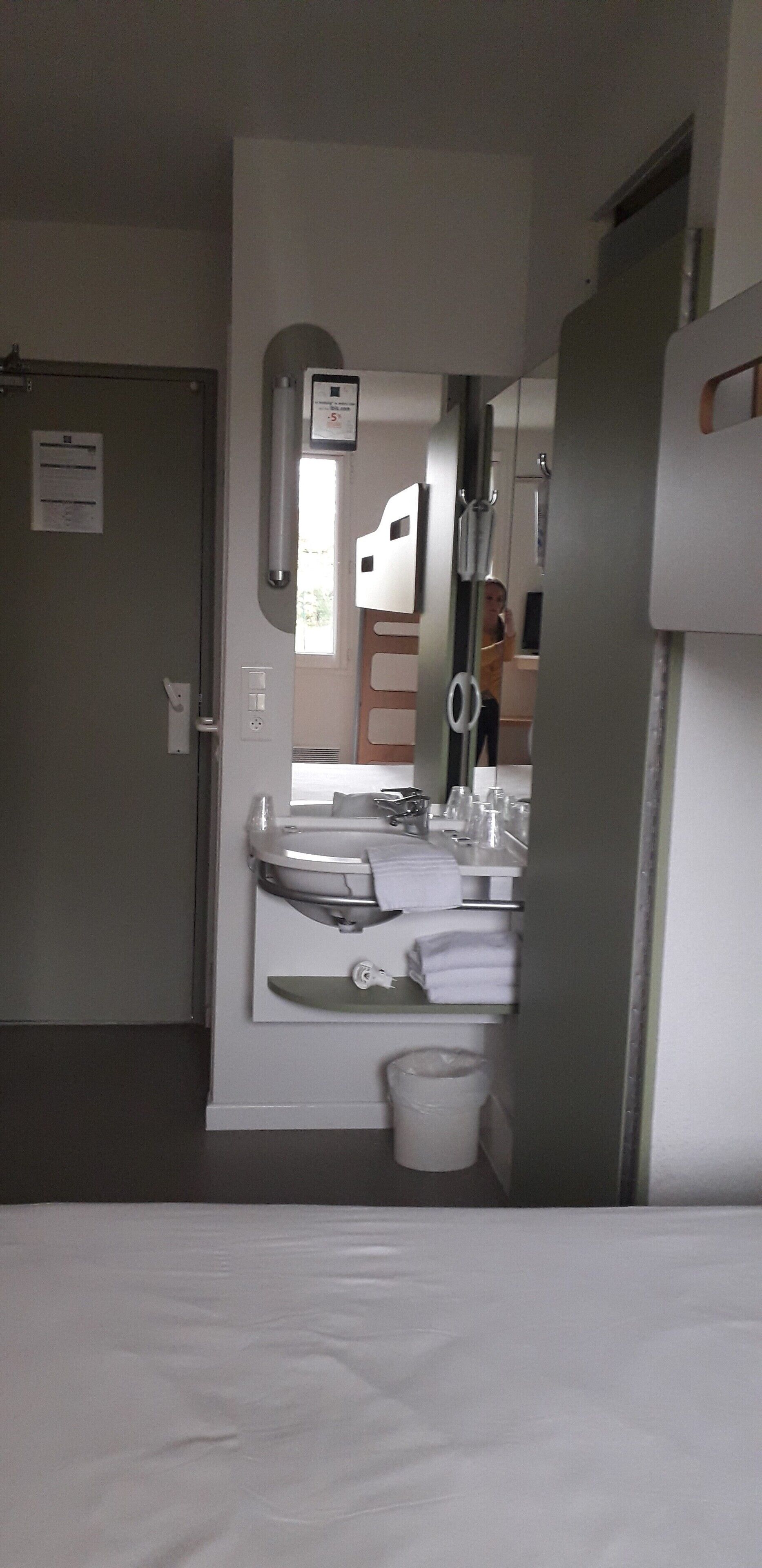 Un baño de hotel con lavamanos, espejo, toallero y un cubo de basura.
