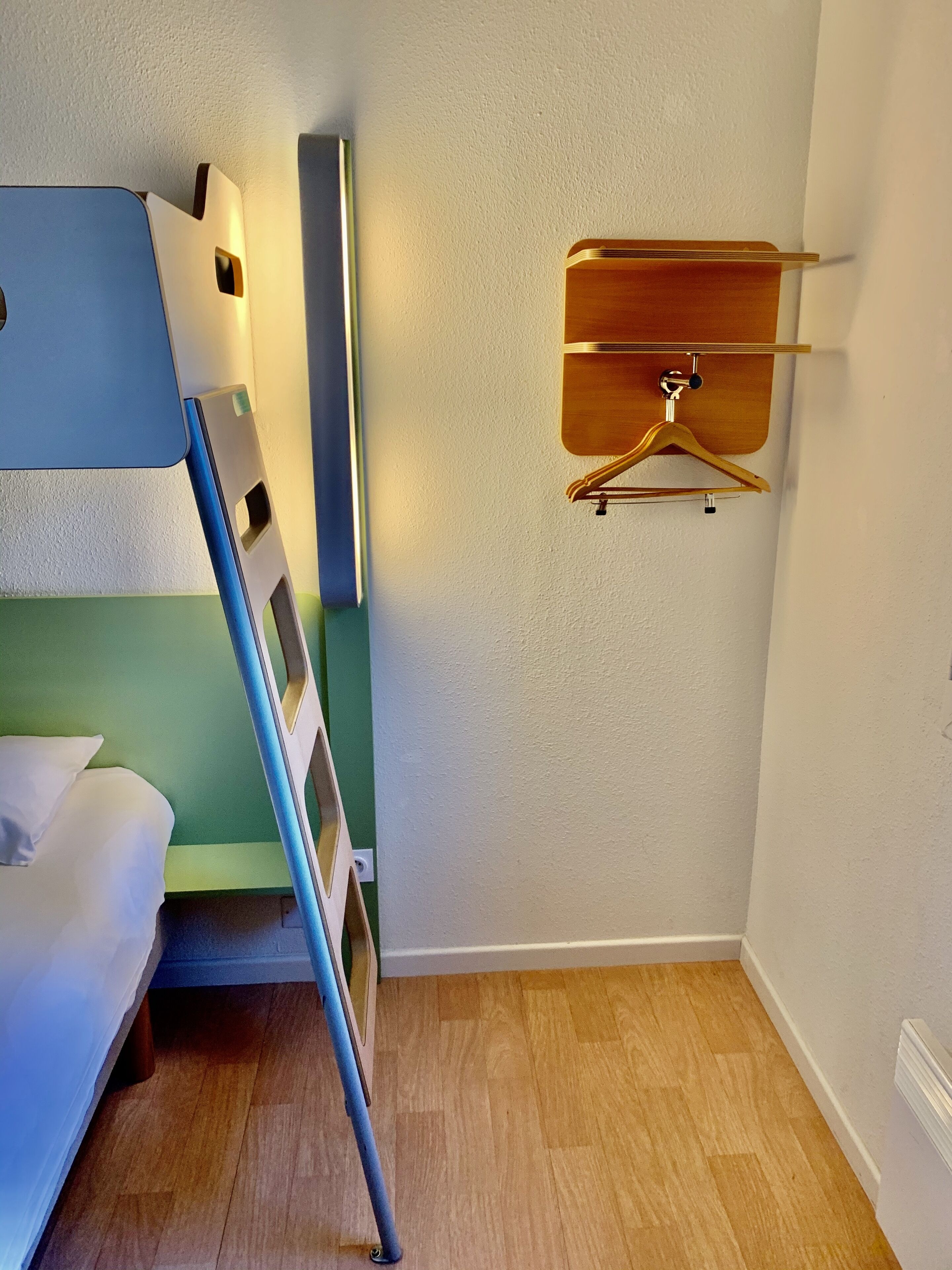 A small, compact room with a bunk bed, a wooden hanger, and a light switch on the wall.
