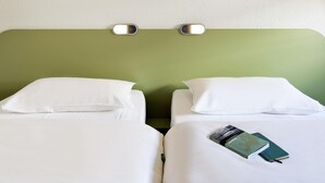 Habitación de hotel con dos camas, ropa blanca, cabecero verde y una lámpara fijada a la pared.
