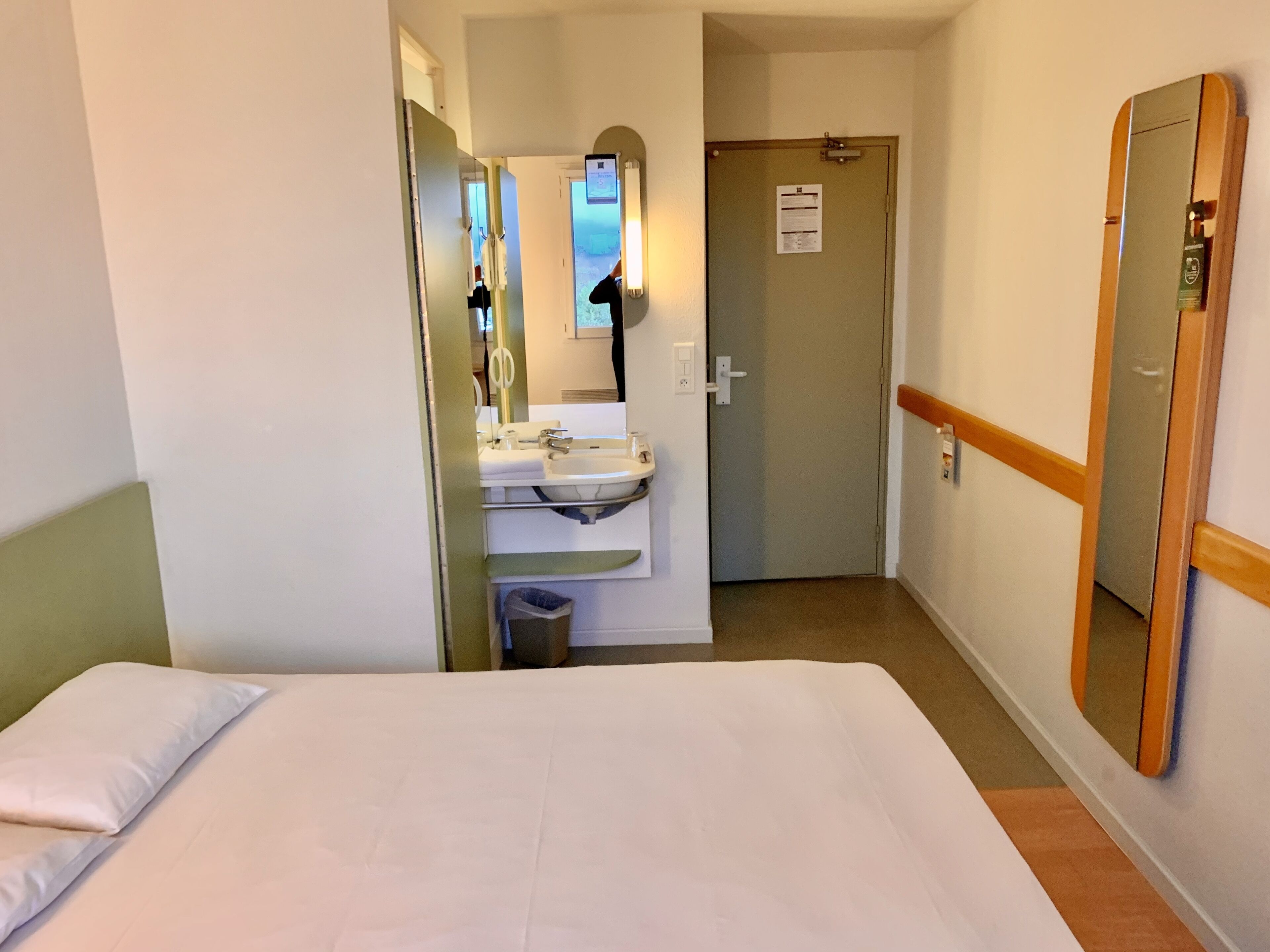 A hotel room with a bed, a bathroom with a sink and mirror, and a door leading to another room.