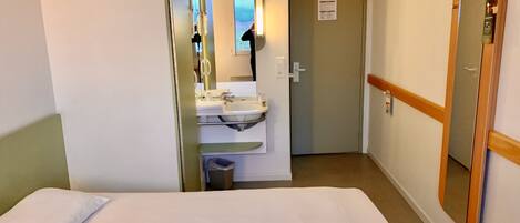 Habitación de hotel con cama, baño con lavabo y espejo, y una puerta que da a otra habitación.