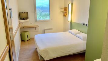 A bedroom with a bed, a television on a stand, a window, a small stool, and a green wall.