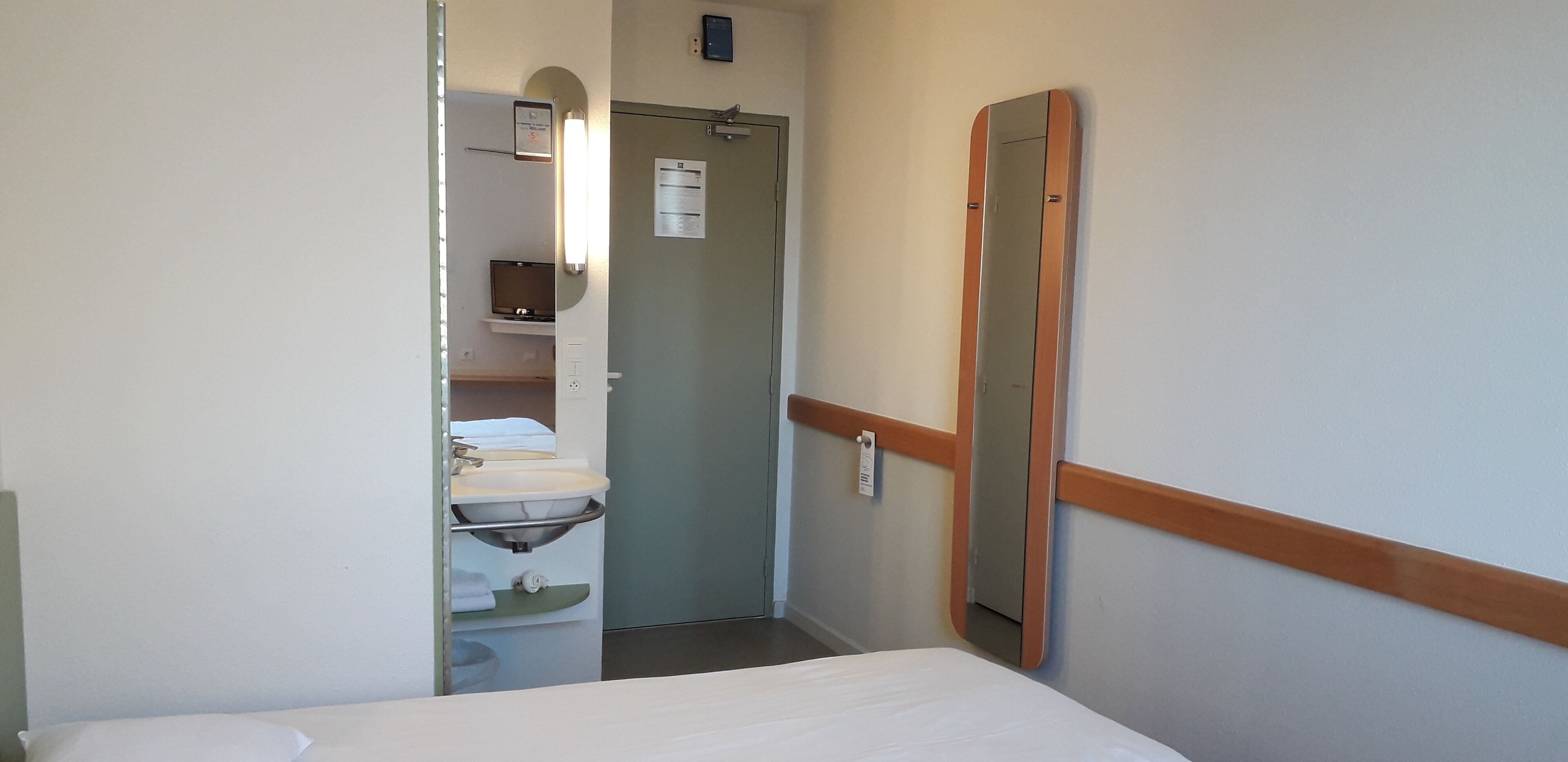 Una habitación de hotel con cama, baño con lavamanos y espejo.