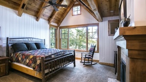 Un dormitorio con cama de madera, una mecedora, chimenea y ventanas amplias.