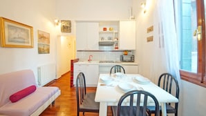 A compact kitchen with white cabinets, a dining table set for two, and a sofa with a red cushion. - DolceVita Apartments N. 408 (Venice)