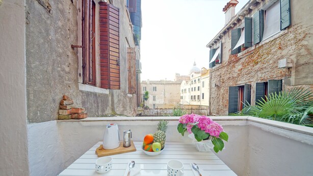A balcony with a white table set with cups, spoons, and a fruit bowl. - DolceVita Apartments N. 408 (Venice)