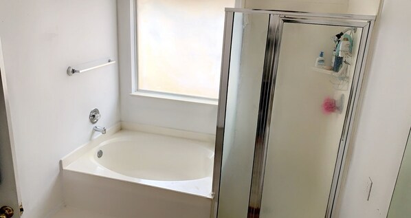 A bathroom with a white bathtub, a window, and a glass shower enclosure.