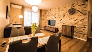 A dining area with a brick wall, a television, and a wooden dining table with chairs. - Baltic Apartments - Apartament Aurora (Swinoujscie)