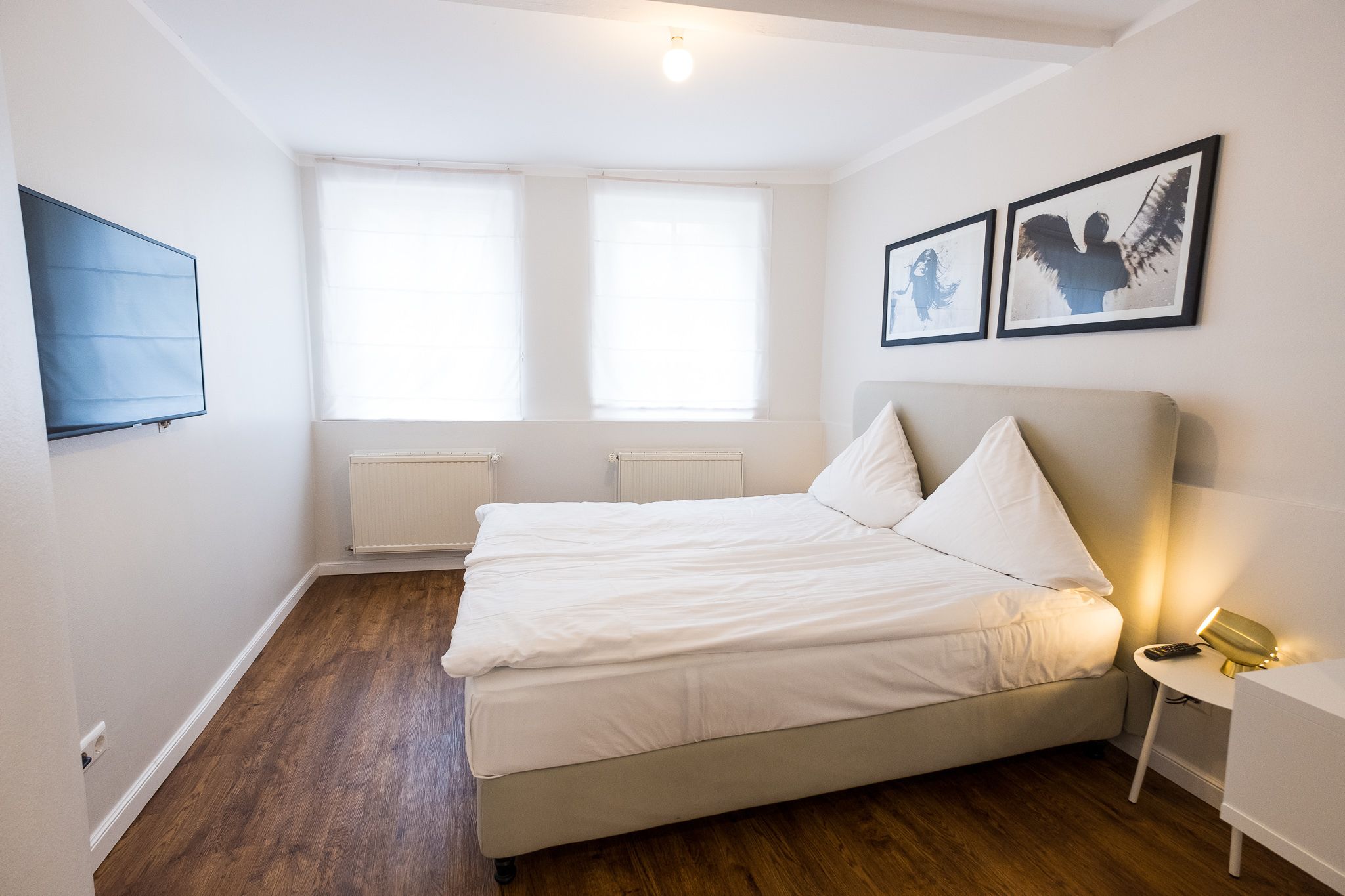 Un dormitorio con cama, televisor y dos ventanas.