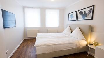 Un dormitorio con cama, televisor y dos ventanas.