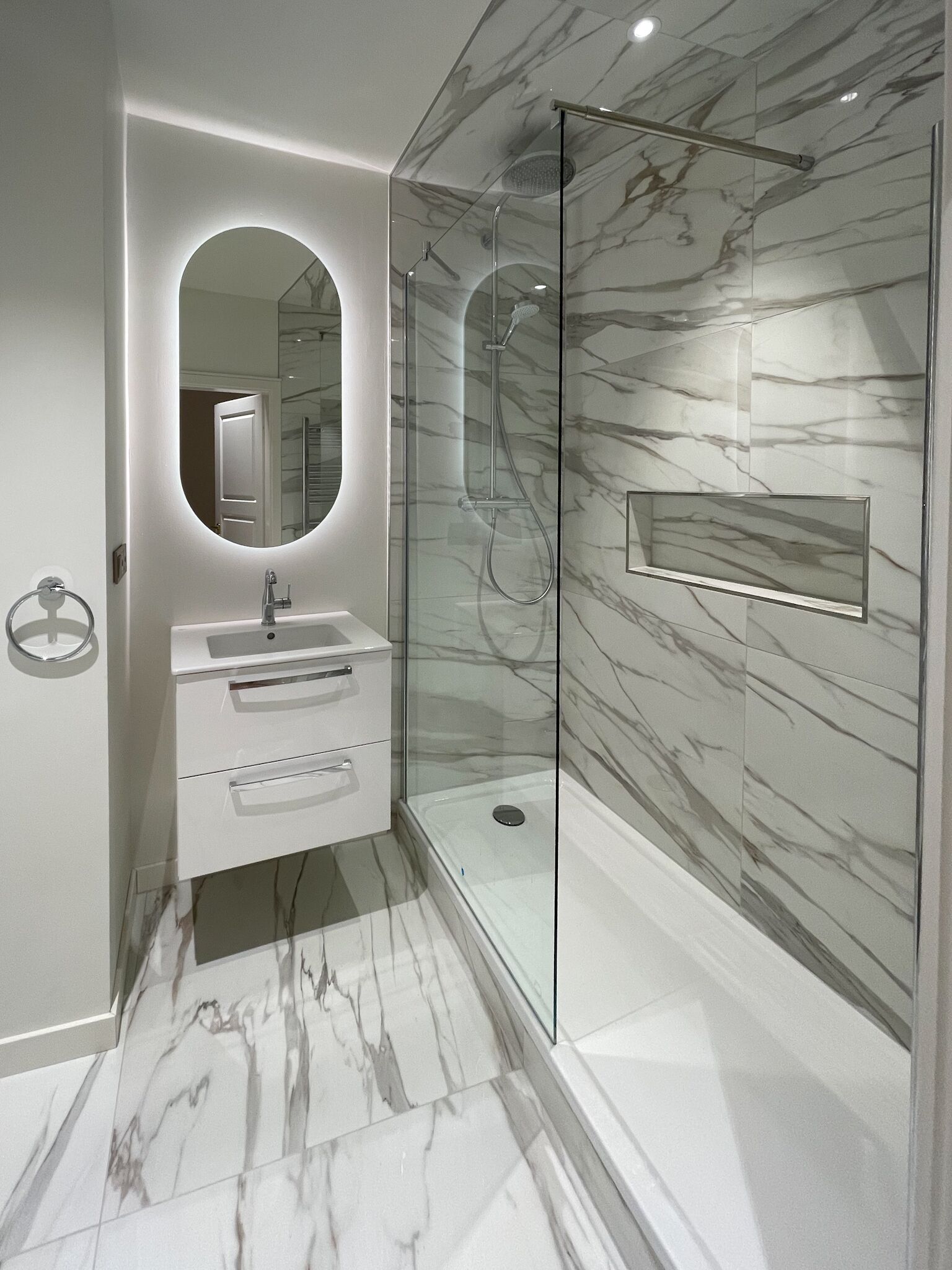 A modern bathroom with a glass-enclosed shower, a vanity with a mirror, and marble-patterned walls.