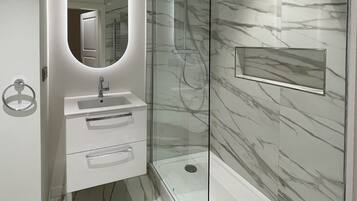 A modern bathroom with a glass-enclosed shower, a vanity with a mirror, and marble-patterned walls.