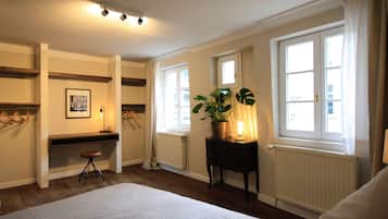Un dormitorio con cama, escritorio, silla, radiador y ventana con cortinas.